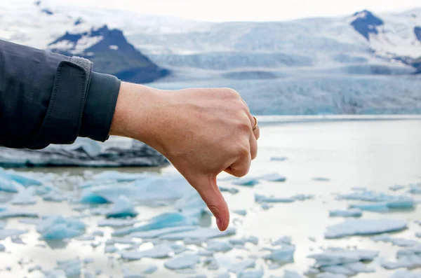 Person hand showing thumb down emotion towards climate change and global worming. Melting glacier on background.