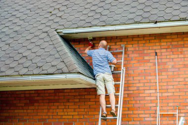 Man home owner working repainting house with paint brush and white paint outdoors in summer.