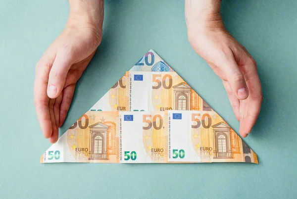 Pyramid scheme or Ponzi scheme concept. Euro money folded as pyramid shape and man showing on blue background, studio shot.