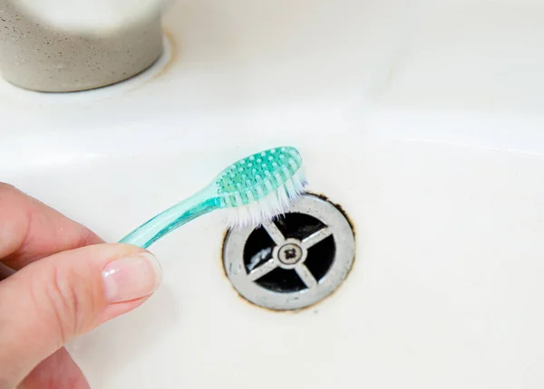 Close up view of woman hand cleaning bathroom sink with toothbrush. Home cleaning hack, fits small spaces to clean off mould and dirt.