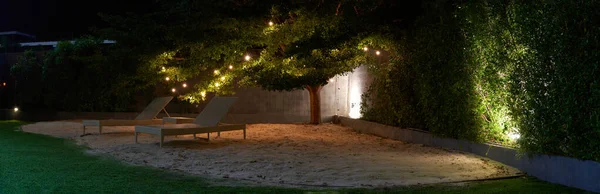 beach chair on sand and lawn under trees at night