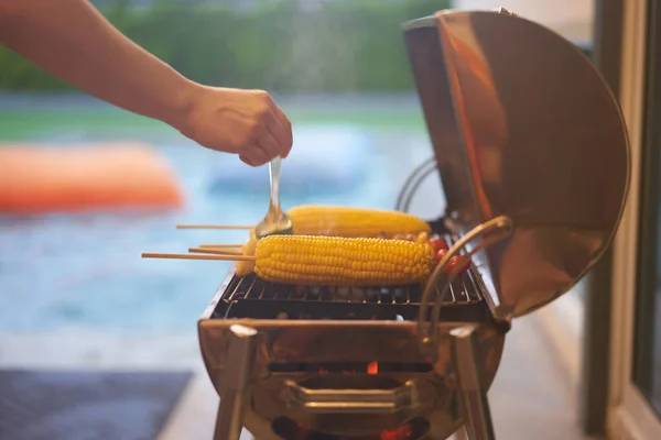 corn barbecue with motion blur hand brush dipping sauce on blur swimming pool party background