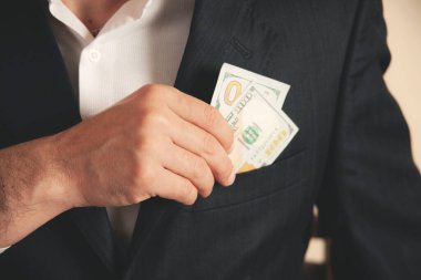 Adam gri arka planda takım elbisenin cebine para koyuyor.