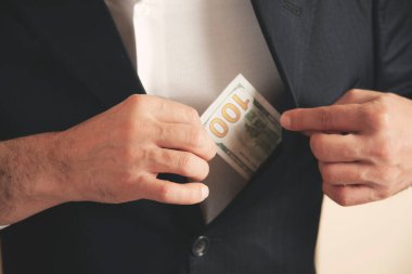 Adam gri arka planda takım elbisenin cebine para koyuyor.