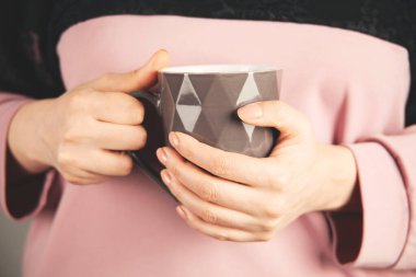 Bir fincan çay ya da kahve tutan bir kadın.