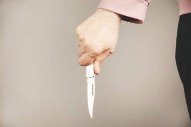 Gri arka planda eli bıçaklı bir kadın.