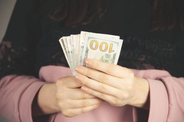 Genç bir kadın gri arka planda para dağıtıyor.