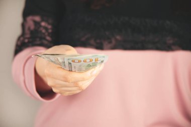 Genç bir kadın gri arka planda para dağıtıyor.