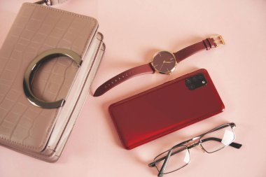 Kadın çantası ve telefon pembe masada.