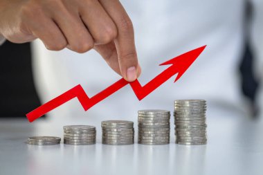 Yatırımcıların ya da iş adamlarının elleri kırmızı okları bozuk para yığınının üzerinde, aşağıdan yukarıya doğru tutarlar. Gayrimenkul büyümesi, mali planlama, hesap yönetimi ve başarı grafikleri kavramı.