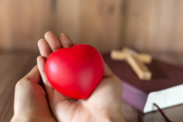 A red heart symbol on hand and a cross on the Scriptures. A blessing from God with the power and power of holiness, which brings luck and power of religion.