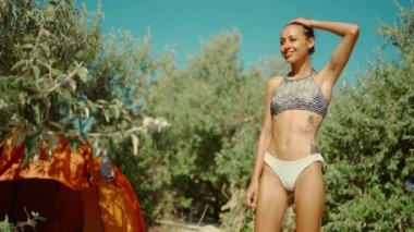 Bikinili güzel melez kadın kumlu sahilde güneşli bir sabahın tadını çıkarıyor. Esneme hareketleri yapan bir kadın çadırda kayıp düşüyor.