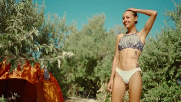 Zrelaksowana piękna mieszana kobieta rasy w bikini ciesząca się słonecznym porankiem na kempingu na piaszczystej plaży. Kobieta rozciągająca się w namiocie — Wideo stockowe