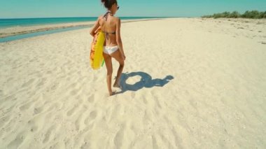 Arka plan yavaş çekim seksi, ince kadın beyaz deniz sahilinde büyük şişirilebilir ananas yüzüğüyle yürüyor. Yaz tatilinde tropik adada beyaz bikinili güzel popo.