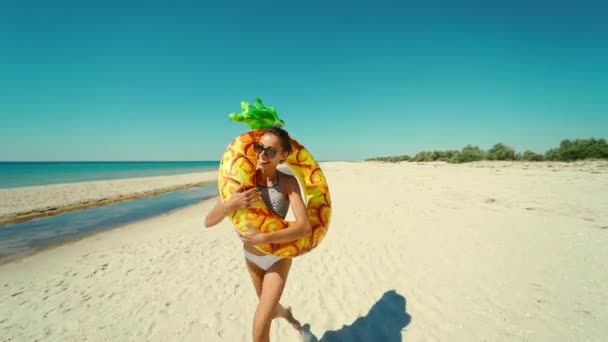 Allegro felice giovane donna attraente corre sulla spiaggia di sabbia soleggiata vuota con ananas gonfiabile giallo anello galleggiante in estate viaggi mare — Video Stock