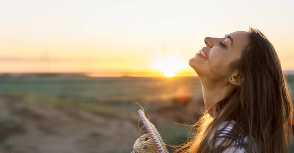 Sivukuva muotokuva iloinen nainen nauttii auringonlaskun aikaa niityllä — kuvapankkivalokuva