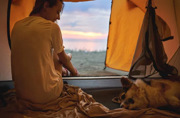 Woman just waking up in camping tent, looking at her pet sleeping dog Welsh Corgi — Stock Photo, Image