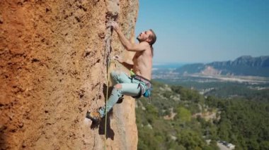 Güçlü kaya tırmanışçılarının 4k yavaş çekimi zorlu bir rotayla dikey kayalıklara tırmanır. Atletik tırmanışçı elle sert bir hareket yapar, uzanıp kayalara tutunur ve halatı kesmeye çalışır.