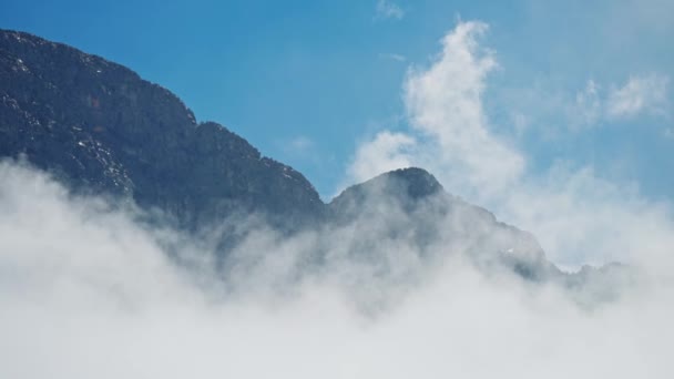 Τεράστια ψηλή βραχώδης κορυφή στο μπλε φόντο του ουρανού που περιβάλλεται από σύννεφα. όμορφο βουνό κορυφογραμμή σε ηλιόλουστη μέρα με μεταβλητό καιρό. — Αρχείο Βίντεο