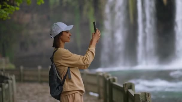 Atractiva mujer sonriente turista haciendo selfie en el teléfono móvil en el fondo de la cascada Duden inferior en Antalya. Punto de vista famoso y lugar turístico en Turquía. — Vídeo de stock