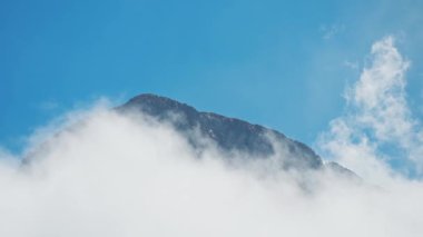 Mavi arka planda yüksek dik kayalık dağ sırtı hareket eden bulutlarla çevrili. Güneşli bir günde, değişken havayla güzel bir dağ. Doğanın inanılmaz güzelliği
