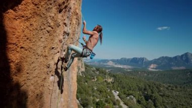 Güçlü ve kaslı kaya tırmanışçıları dik kayalıklarda halatla tırmanırlar. Çıplak gövdesi olan yakışıklı bir adam yükseklikte ipe tırmanıyor ve vücudunun mükemmel şekillerini gösteriyor.