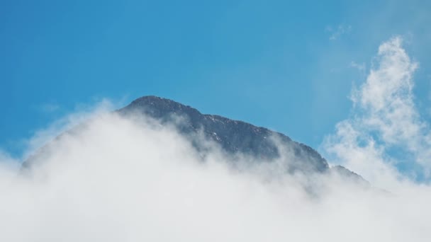Високий крутий скелястий гірський хребет на фоні блакитного неба, оточений рухомими хмарами. красива гора в сонячний день зі змінною погодою. дивовижна краса природи — стокове відео