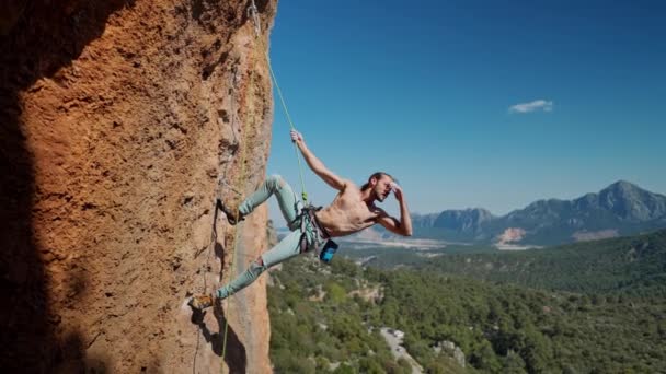 Fort et musclé grimpeur accroché à la corde sur la falaise verticale. bel homme avec torse nu posant tout en accrochant à la corde à l'altitude et montrant des formes parfaites de son corps de sport — Video