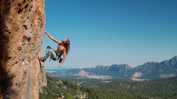 Повільний рух красивого тіла людини скелястий альпініст висить на мотузці на вертикальній скелі, дивиться вгору і робить високий хід вгору і рухається тримає камінь вручну — стокове відео