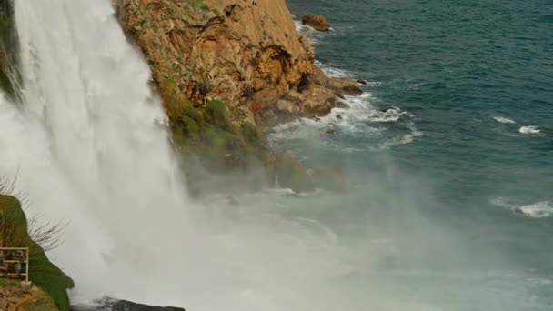 Powolny film z wodospadem Low Duden w Antalyi w Turcji. Wspaniały i potężny strumień wody wpada do burzliwego turkusowego morza z falami, które rozbijają się o skały przybrzeżne — Wideo stockowe