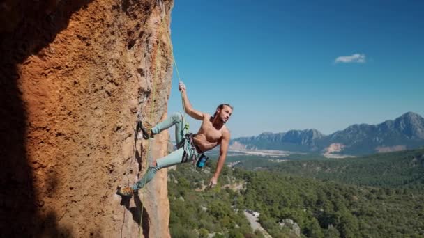 強く筋肉質のフィットロッククライマーは垂直崖のロープにかかっています。高さにロープをかけながら裸の胴を持つハンサムな男と彼のスポーツボディの完璧な形状を示しています — ストック動画
