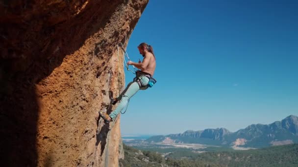 Young fit muscular attractive man rock climbing outdoors, preparing to rappel on rock face after successful climbing — Stock Video