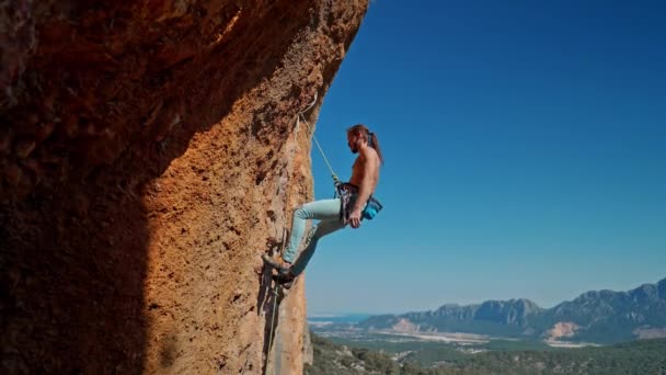 强壮英俊男子攀岩者的侧视图从顶部的垂直悬崖上下降。岩石山脊，蓝天清澈。土耳其的健康生活方式和户外活动. — 图库视频影像