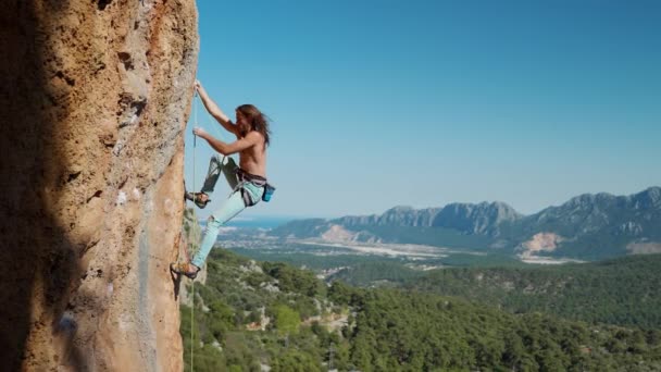有吸引力的强壮而健康的男人攀岩者，长发挂在悬崖峭壁上，向上看。美丽的风景，山脊多岩石，背景蓝天清澈 — 图库视频影像
