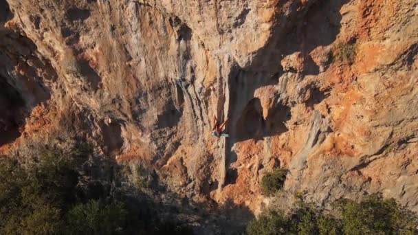 Punto de vista aéreo desde el dron de hombre musculoso fuerte sube desafiante ruta de escalada en roca. escalador alcanza asideros y hace largo movimiento duro — Vídeo de stock