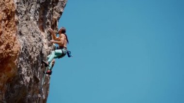 Açık havada kaya tırmanışı anları. Dikey yamaçta zorlu rotada atletik kaya tırmanışçısı eğitimi. Adam iple tırmanır, hareketleri ayrıştırır ve kaya yüzeyine ulaşır.