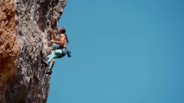 Momentos de escalada al aire libre. atlético hombre escalador de roca de entrenamiento en la ruta difícil desafiante en acantilado vertical. hombre sube por la cuerda, analiza los movimientos y alcanza sostiene en la cara de roca — Vídeo de stock