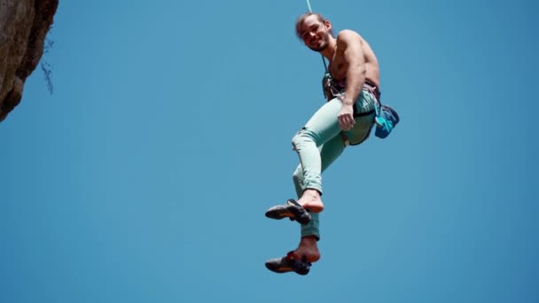 Side view of athletic handsome smilking man rockclimber descends from cliff on top rope. clear blue sky on background. healthy lifestyle and sport activity outdoors in Turkey. — Stock Video