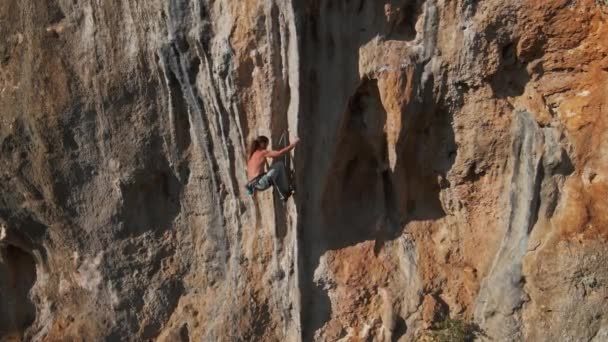 In Zeitlupe aufgenommene Drohnenaufnahmen zeigen einen starken Bergsteiger, der auf einer harten Route auf einem senkrechten Felsen mit riesigem Tuff klettert. Bergsteiger unternimmt mehrere schwierige Anstrengungen und Bewegungen, um sich zu halten — Stockvideo