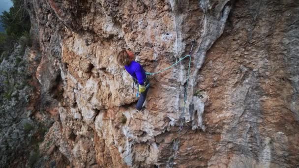 Stark flicka bergsklättrare klättrar på överhängande crag. kvinna vilar på utmanande överhängande klättringsrutt, ger vila för händer och ta av sig jackan. — Stockvideo