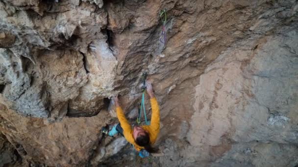 トップビュー強力な熟練したロッククライマーの映画的なスローモーションは、岩の崖の上に登る。人は困難かつ困難な努力と動きをし. — ストック動画