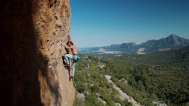 Güçlü atletik adam kaya tırmanışçısının 4k yavaş çekimi zorlu bir rotayla dikey kayalıklara tırmanır. Dağcı dikkatli adımlar atar ve dinlenmek için iyi bir konuma ulaşır.