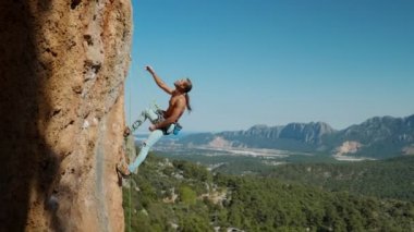Yakışıklı, güçlü ve formda bir kaya tırmanışçısı uzun saçlı, dikey kayalıklarda asılı duran, yukarı bakar ve elleriyle gösterir..