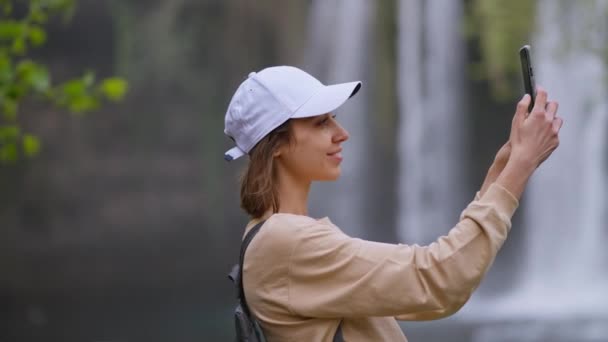 Приваблива посміхається жінка-туристка, яка робить самовідтворення на мобільному телефоні на Уотерфолл фоні в Анталії. Знаменита точка зору і туристичне місце в Туреччині. — стокове відео