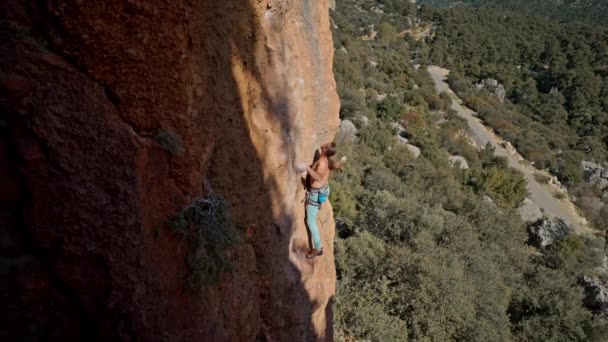 Vista lateral superior hombre fuerte en forma de roca escalando el lado de una montaña. escalador se pone mosquetón de tiro rápido. cinemático cámara lenta momento de escalada en roca — Vídeo de stock