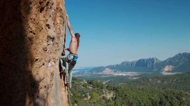 4k cámara lenta del hombre atlético sube una roca vertical con cuerda, escalada de plomo. silueta de un escalador sobre un fondo de montaña y cielo azul. — Vídeo de stock