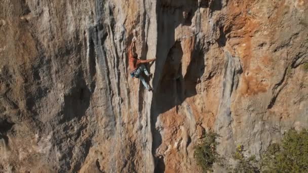 Lassított felvételeket az erős férfi sziklamászóról, amint nehéz úton mászik fel függőleges sziklaszirten hatalmas tufával. mászó tesz néhány kemény trükkös erőfeszítések és mozgások kitartani — Stock videók