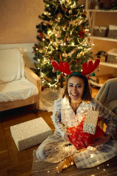 Søt dame ved juletreet, med gavebokser, med reinsdyrgevir på hodet – stockfoto