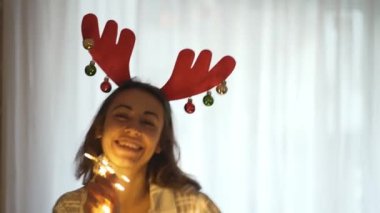 Ren geyiği boynuzu takan genç ve güzel bir kadın. Evde Noel ışıklarıyla dans ediyor.