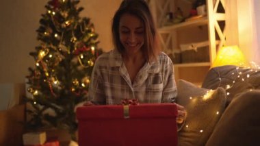 Portre, Noel 'de evde Noel kutlaması için hediye kutusunu açan aşırı mutlu komik bir kadın. Güzel pijama giyen sürpriz kız hediye kutusu arıyor.